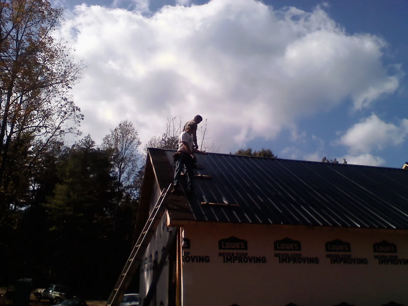 Roofer fastening dark metal panels high against a cloudy sky, from a Roof Inspection job in Alexandria